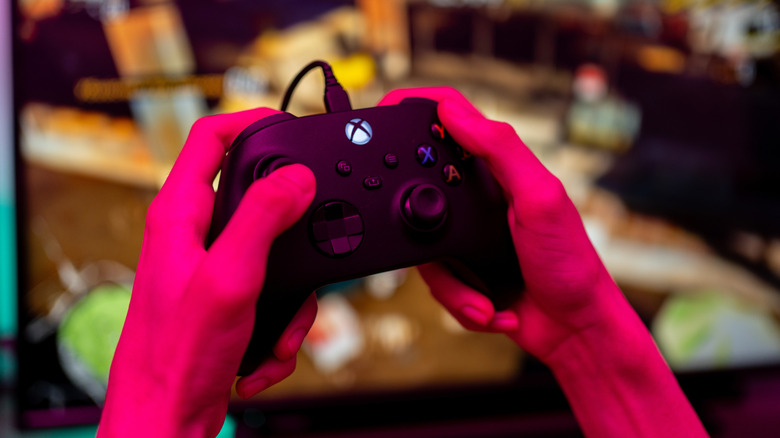 Hands using wired Xbox controller in pink lighting