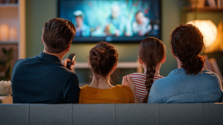 A family sits on a couch and watches TV.