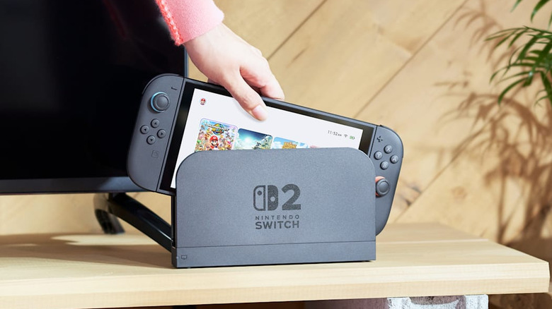 Hand placing Nintendo Switch 2 console into the dock on a wooden table.