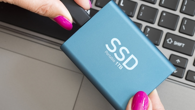 Woman holding a blue 1 TB portable SSD against a laptop's keyboard