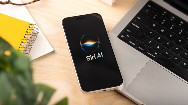 iPhone showing Siri AI logo while on top of a table with laptop and notebook