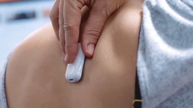 A woman placing a posture tracker on her back.