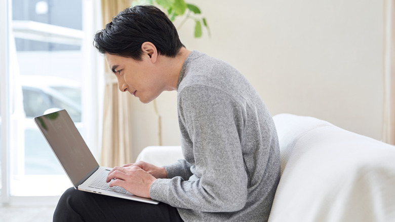 A man slouching on a sofa while using a laptop.