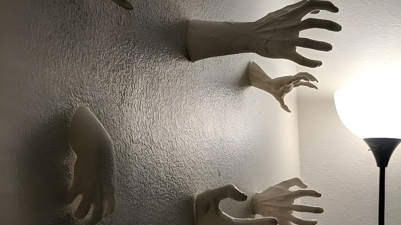 3D printed human hands reaching out of a white wall