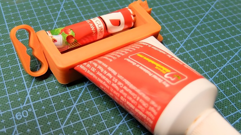 An orange 3D printed Toothpaste squeezer with a twiting mechanism halfway down a tube of toothpaste on a craft matt.