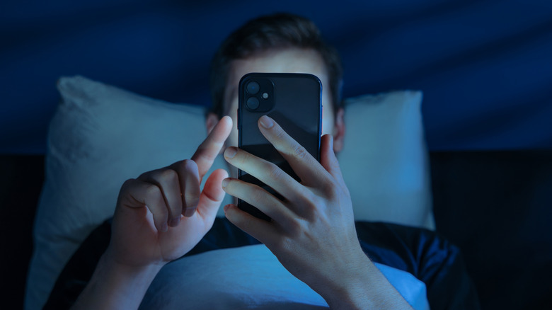 A man in bed in the dark looking at his smartphone