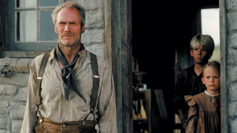 Will Munny (Clint Eastwood) stood outside his house while children stand in the doorway in Unforgiven