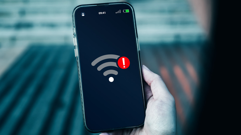A person looking at their phone with a Wi-Fi symbol showing a low Wi-Fi signal with an exclamation mark