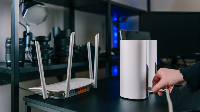 A traditional Wi-Fi router lying beside a mesh Wi-Fi system satellite that is connected to an Ethernet cable