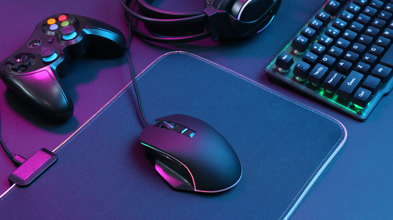 Neon lights shining on a computer mouse, RGB keyboard, game controller, and headset against a dark background.