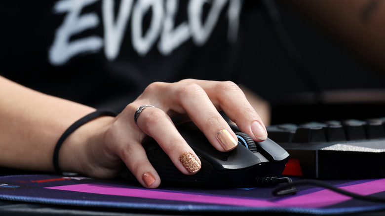 A hand with painted fingernails using a mouse on a pink and purple mousepad.