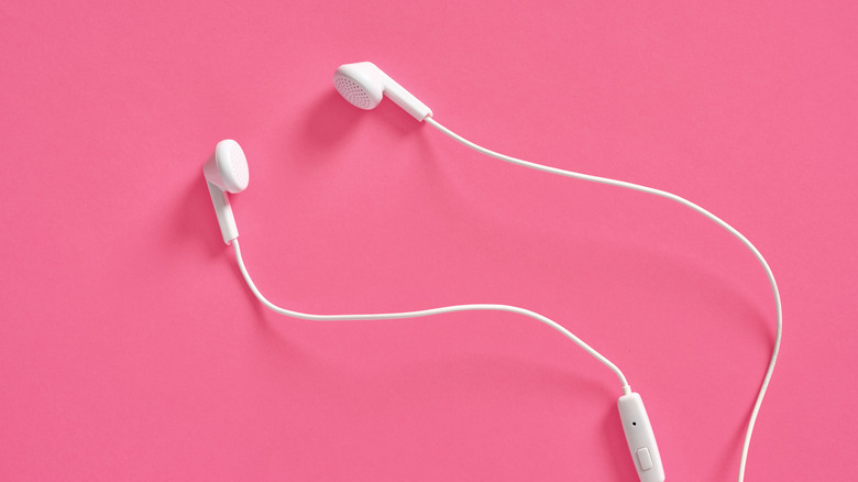 White wired earbuds against a pink background.
