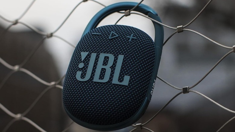 The JBL Clip 4 attached to a chain-link fence by its carabiner hook.