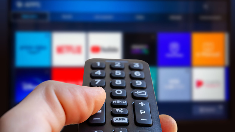 A human hand holds a remote control while it is pointed at a smart television, the contents presented on the screen are too blurry to make out fully