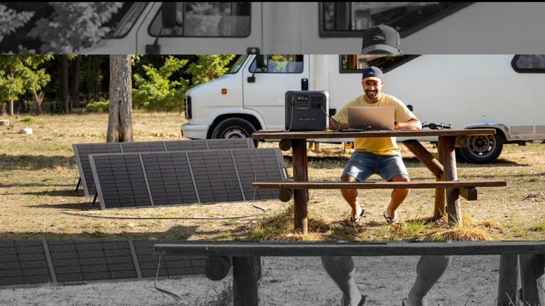 Bluetti power stations with solar panels powering a laptop, with an RV in the background