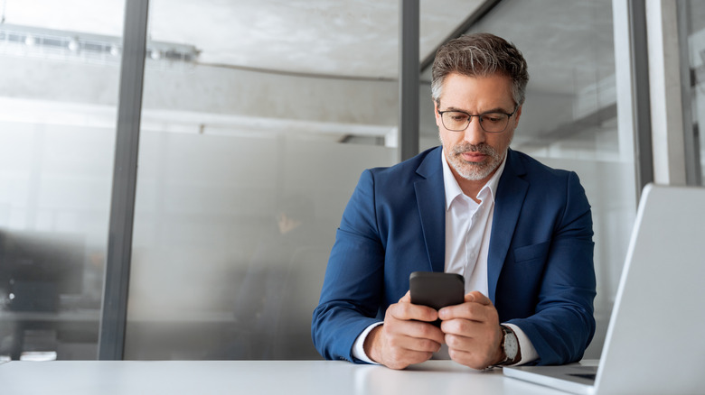 Businessman in suit using phone for business work in office.