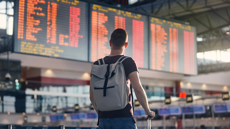 A person in an airport looking at the departure information screens that list several delayed flights.