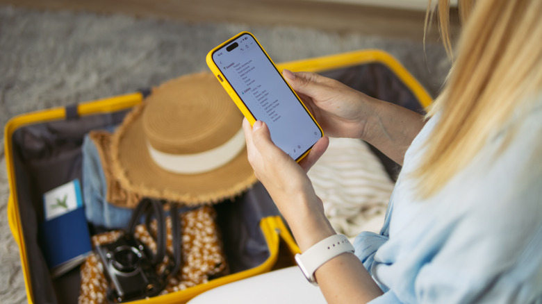 Person looking at a checklist on their phone while packing their luggage