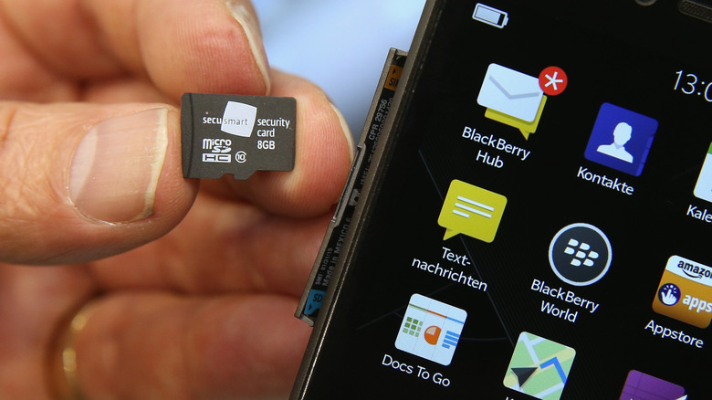A person holding a microSD card beside a smartphone.