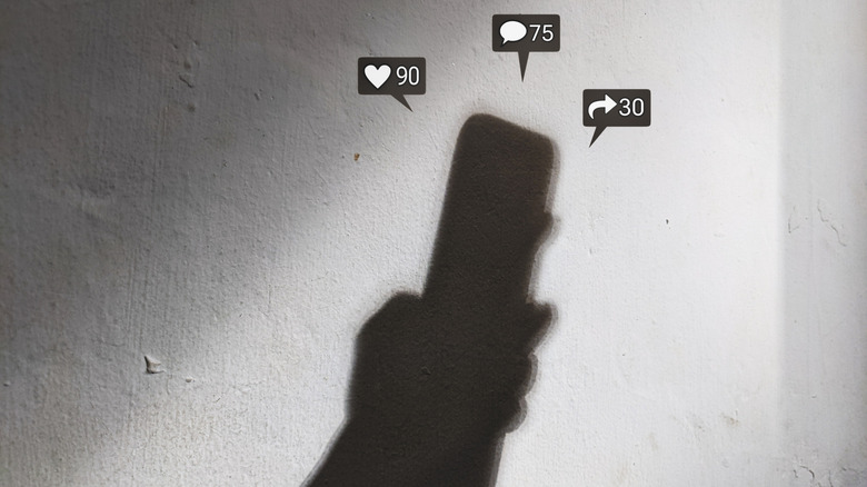 A shadow of a hand holding a smartphone with notification graphics above it.
