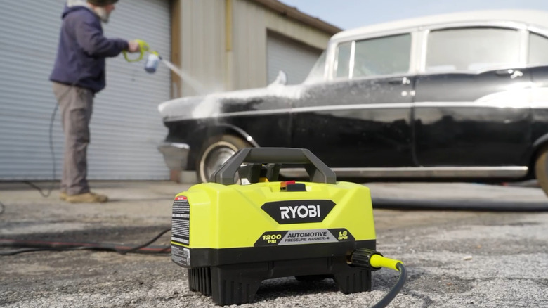 A close up of the Ryobi Pressure Washer device with a person using it on a vehicle in the background