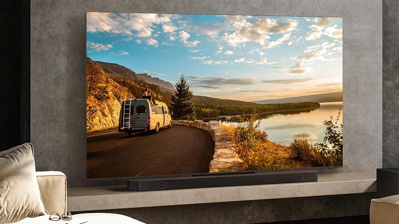 Samsung HW-Q990C Soundbar hanging on a wall underneath a television while an orchestra plays on screen
