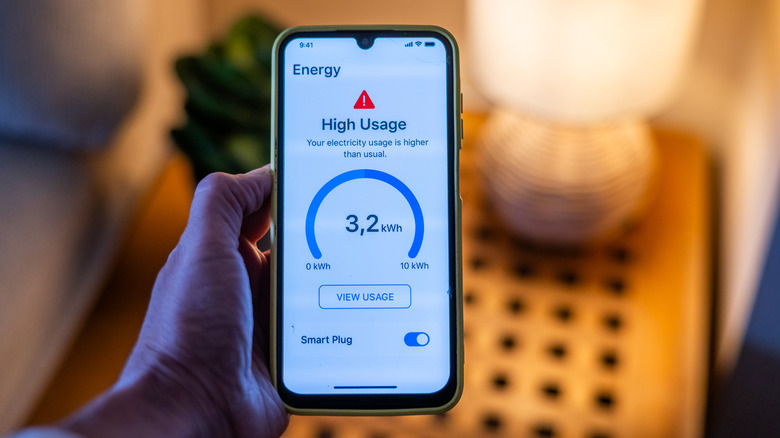 A hand holding a smartphone with a high energy usage warning from a smart plug