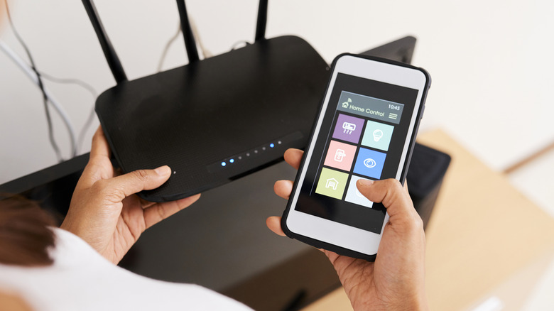 Close up of a person's hands using a smartphone to control a Wi-Fi router