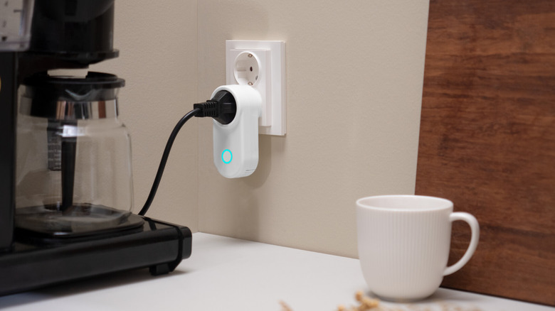 A coffee pot attached to smart plug on a counter with a white mug