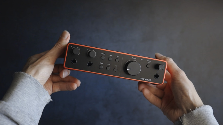 A pair of hands holding a Focusrite Scarlett 2i2 audio interface against a black background.
