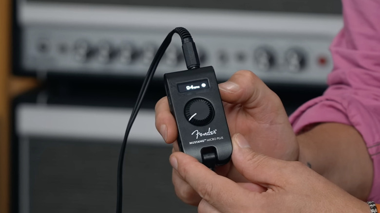 A close up of a pair of hands holding the Fender Mustang Micro Plus headphone amp.