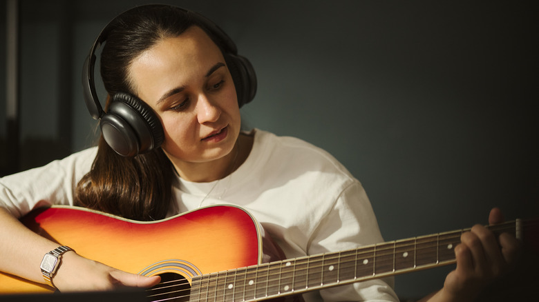 A woman wearing black headphones playing an acoustic guitar.
