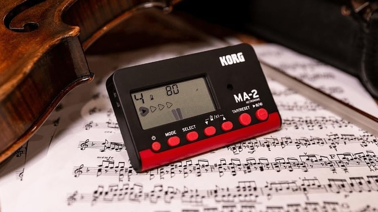 A black and red Korg MA-2 metronome on top of some sheet music and beside a violin.