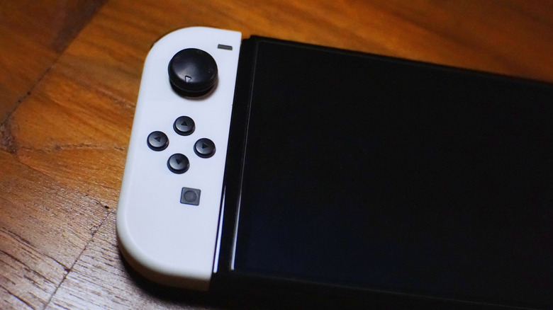 A Nintendo Switch with a white Joy-Con sitting on what appears to be a wooden floor or table