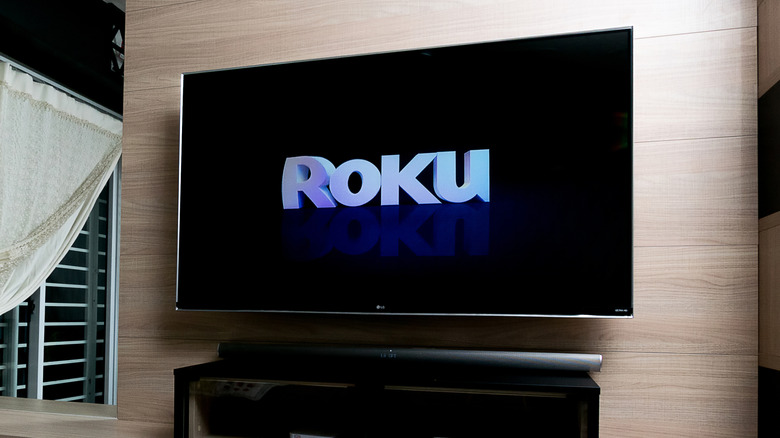 A large television attached to the wall inside of a home, the television is displaying the Roku logo