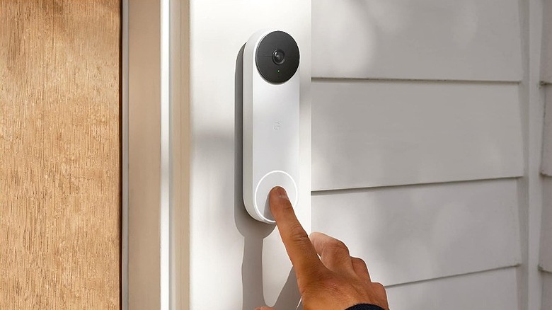 Finger pressing a video doorbell mounted beside a door.