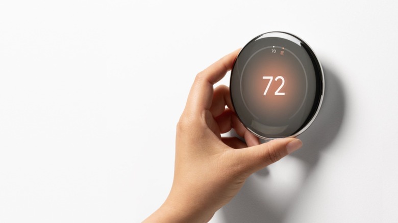 Hand touching a thermostat showing 72 degrees Fahrenheit temperature.