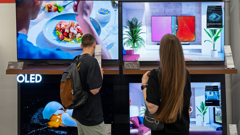 A couple looks at a wall of OLED televisions in a store