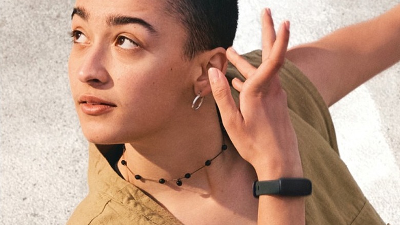 A person touching their ear while wearing the Fitbit Inspire 3 on their wrist.