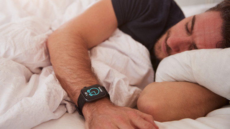 A man sleeping on his side wearing a smartwatch with an alarm going off.
