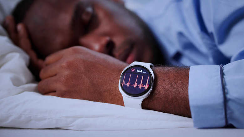 A man sleeping on his side with a smartwatch on his wrist that reads "104 bpm" above a heart monitor.