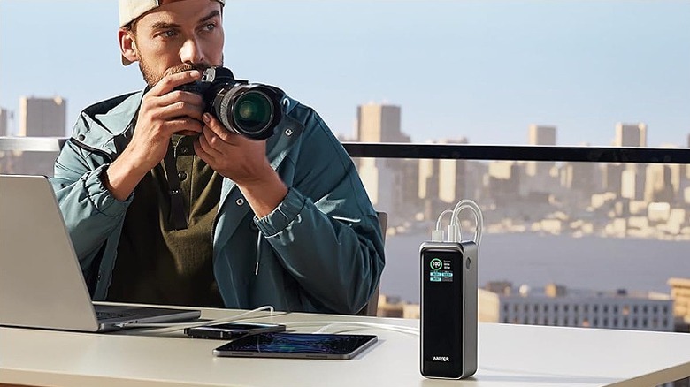 Man clicking a photo with several devices connected to a power bank on the table.