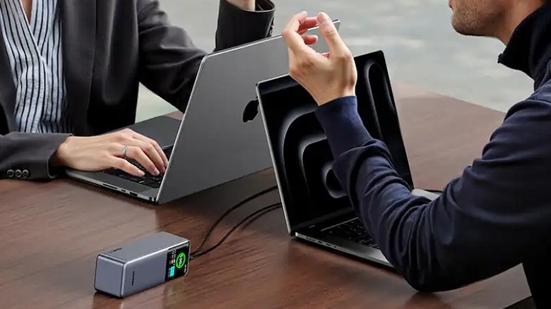 Man and woman sitting across working on MacBooks connected to power bank.