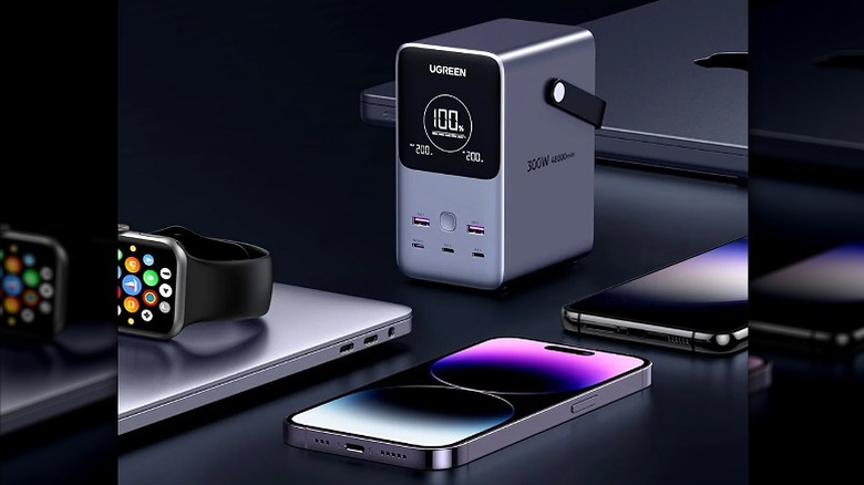 iPhone, Apple Watch, MacBook, and power bank placed on a black surface.