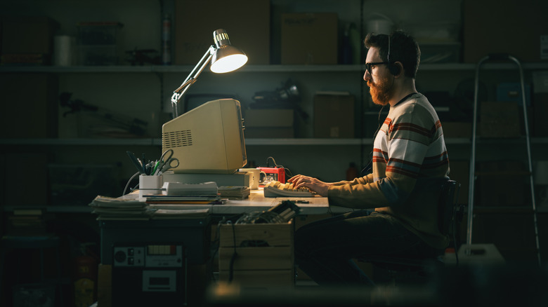 A man wearing retro headphones sits and works at an old '80s PC.