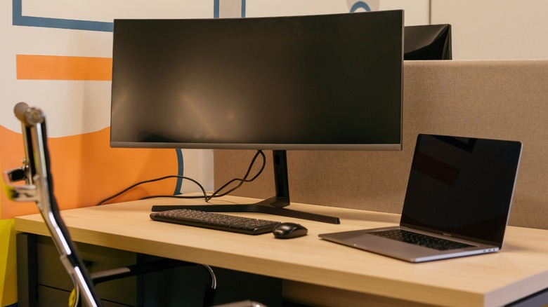 An ultrawide monitor and a laptop on a desk, with the monitor showing just two cables coming out of it