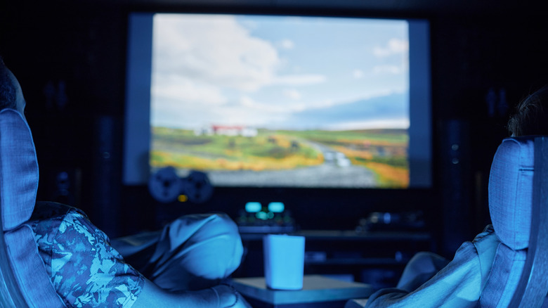 Two people watching a movie together on their projector screen in room bathed in blue light
