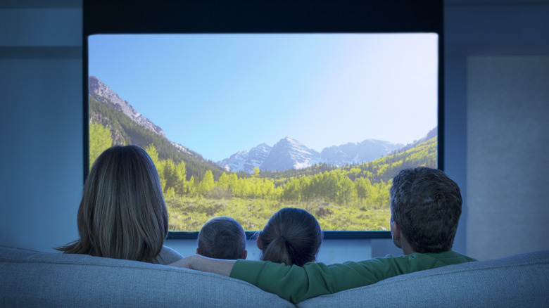A family watching a projector screen showing a clear mountain valley