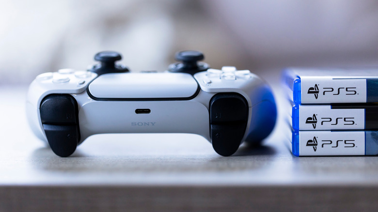 A white DualSense controller next to three PS5 games on a flat surface