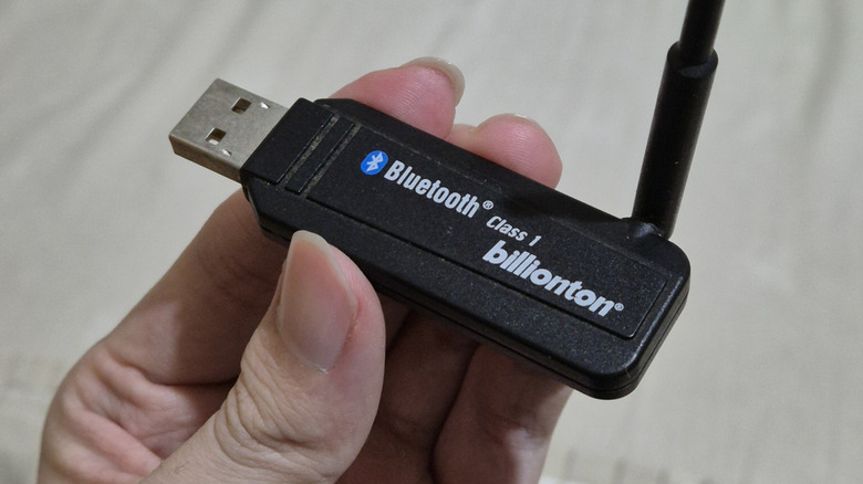 A hand holding a compact Bluetooth USB adapter with an antenna.
